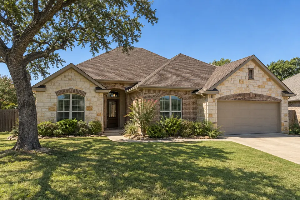A limestone and brick home with a brown architectural shingle roof and a live oak
